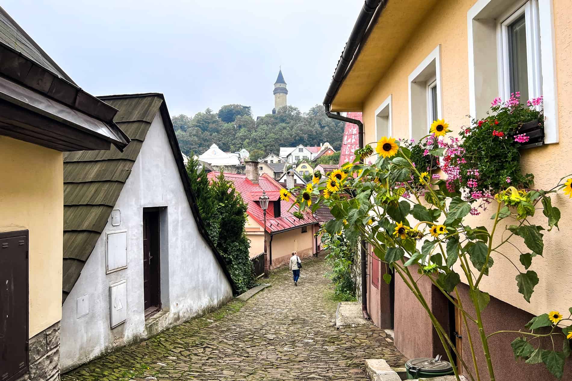 A woman walking through the cobblestoned streets of Štramberk towards the castle tower. 