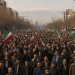 A high-resolution photograph showing a massive daytime protest in Tehran. Thousands of people fill the streets holding Iranian flags and banners, expressing opposition to Israeli airstrikes. The atmosphere is intense but peaceful, with visible unity and national symbolism.