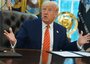 Former President Donald Trump speaks energetically at the Oval Office desk during a live policy discussion, with U.S. and Space Force flags in the background and a binder open in front of him.