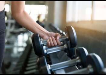 Close-up of a person lifting a dumbbell in a modern gym, emphasizing strength training and fitness