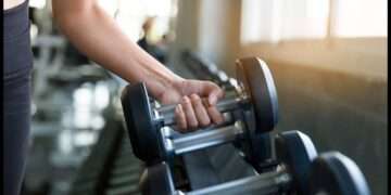 Close-up of a person lifting a dumbbell in a modern gym, emphasizing strength training and fitness