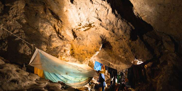 Exploring the World’s Deepest Cave: The Untold Secrets of Krubera (Voronya) in Georgia 1 A speleology expedition base camp set up deep inside Krubera Cave, showing caving gear, tents, and supplies under dramatic rocky formations illuminated by artificial light.