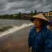 A realistic photograph of Vietnamese families evacuating ahead of Typhoon Kajiki, with buses, soldiers, and storm clouds in the background.
