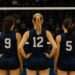 Indy Ignite Brings Global Spotlight to Women's Volleyball 2 Three female volleyball players in navy blue jerseys, showing only their backs and jersey numbers (9, 12, and 5), standing on an indoor court facing the net during a professional match
