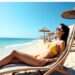 Base Tan Truth: Experts Expose the SPF Myth of Sun Protection 2 A woman sunbathing on a beach chair in a yellow bikini, wearing white sunglasses, with clear blue sky and sea in the background. Photorealistic beach scene