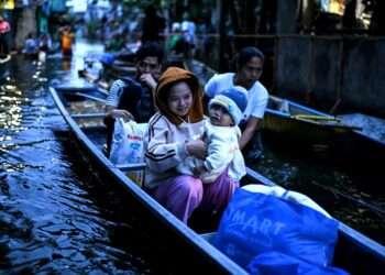 Evacuated families in the Philippines navigating floodwaters by boat after Tropical Storm Bualoi, holding children and emergency supplies.