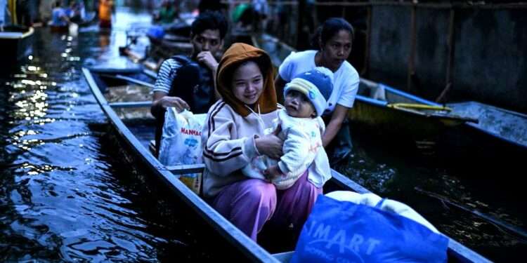 Evacuated families in the Philippines navigating floodwaters by boat after Tropical Storm Bualoi, holding children and emergency supplies.
